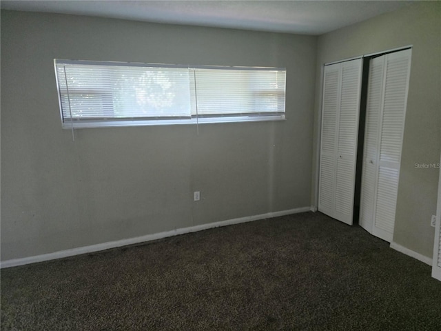 unfurnished bedroom with a closet, baseboards, and dark carpet