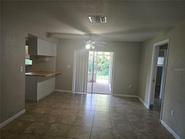 unfurnished dining area featuring a textured ceiling, baseboards, ceiling fan, visible vents, and tile patterned flooring