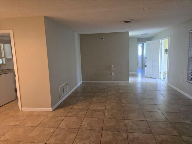 tiled empty room featuring baseboards, visible vents, and a textured ceiling