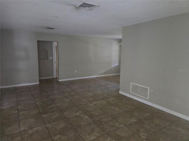spare room featuring dark tile patterned flooring, baseboards, and visible vents