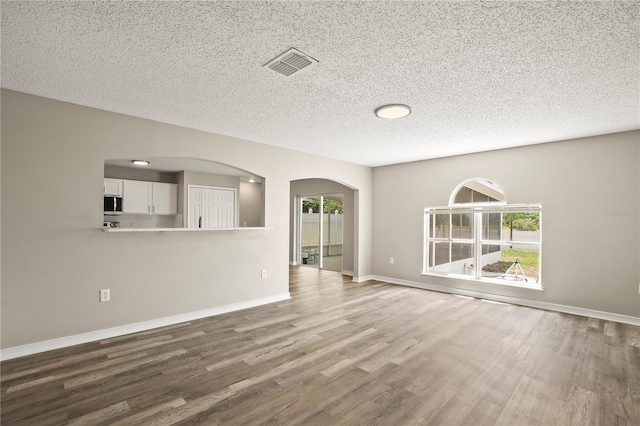 11323 Ivy Flower Loop, Riverview, FL 33578 - unfurnished living room featuring wood finished floors, a textured ceiling, visible vents, baseboards, and arched walkways