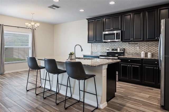 kitchen with stainless steel appliances, dark cabinetry, a sink, light wood-style floors, and tasteful backsplash