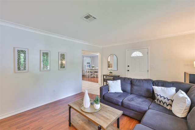 living room featuring baseboards, crown molding, visible vents, and wood finished floors