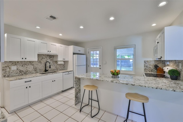 kitchen with a peninsula, a sink, white cabinetry, visible vents, and white appliances