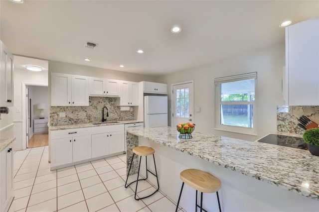 kitchen featuring freestanding refrigerator, visible vents, a sink, a peninsula, and white cabinets