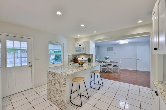 kitchen featuring light tile patterned floors, white microwave, a kitchen breakfast bar, white cabinets, and electric range