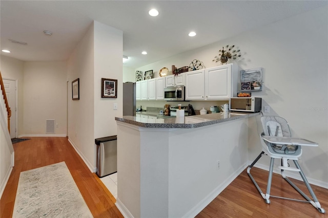 kitchen with recessed lighting, a peninsula, light wood-style floors, stainless steel appliances, and white cabinets