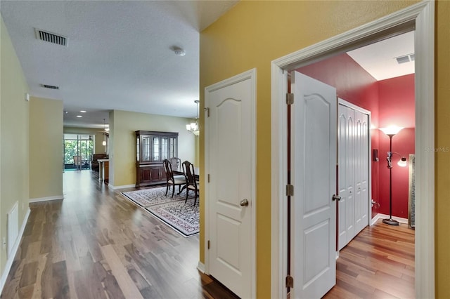 hall featuring an inviting chandelier, visible vents, wood finished floors, and baseboards