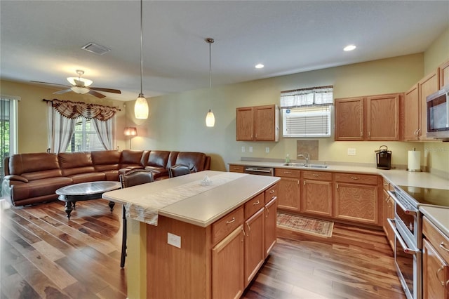kitchen featuring a sink, open floor plan, wood finished floors, light countertops, and appliances with stainless steel finishes