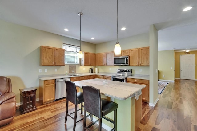 kitchen with a sink, stainless steel appliances, light wood-style flooring, light countertops, and a kitchen bar