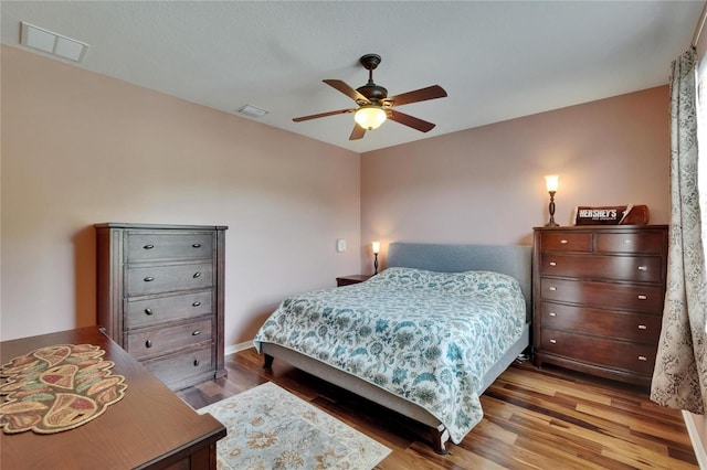 bedroom with baseboards, visible vents, wood finished floors, and a ceiling fan