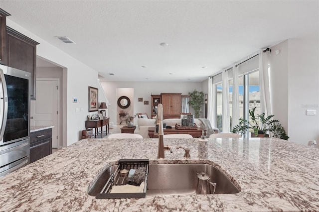 kitchen featuring a sink, dark brown cabinets, light stone countertops, and open floor plan