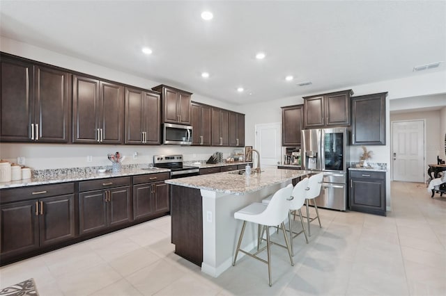 kitchen featuring appliances with stainless steel finishes, a sink, a breakfast bar, light stone countertops, and dark brown cabinets