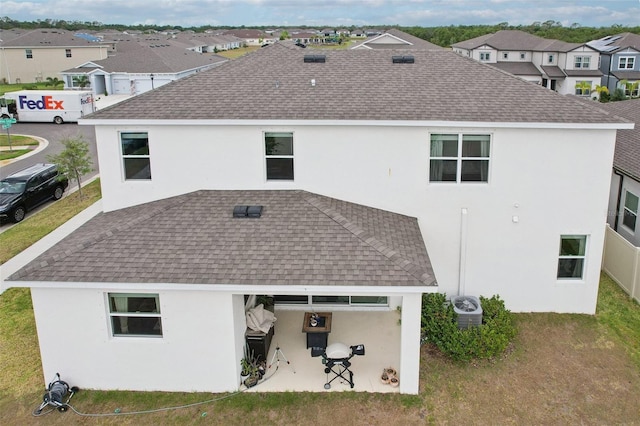 rear view of property featuring a shingled roof, a residential view, stucco siding, a patio area, and cooling unit