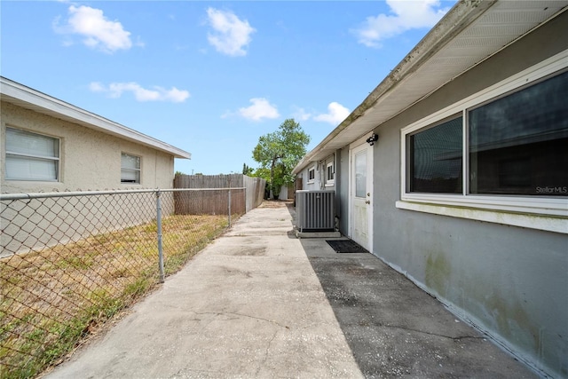 view of side of property with fence, stucco siding, cooling unit, and a patio area