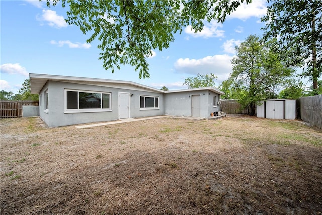 rear view of property with a storage shed, stucco siding, an outbuilding, and a fenced backyard