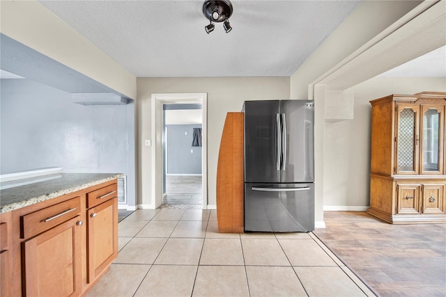 kitchen with freestanding refrigerator, brown cabinetry, visible vents, baseboards, and light stone counters