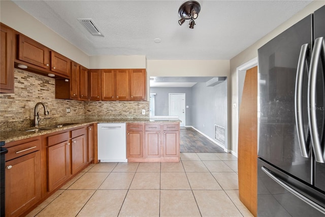 kitchen featuring a sink, freestanding refrigerator, visible vents, backsplash, and dishwasher