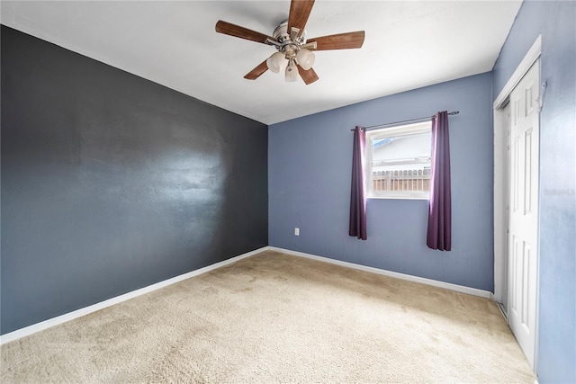 carpeted spare room with a ceiling fan and baseboards