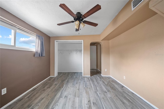 unfurnished bedroom featuring a closet, wood finished floors, baseboards, and arched walkways