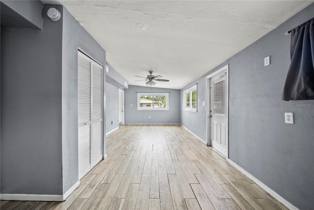 corridor featuring light wood-style floors, baseboards, and a textured wall