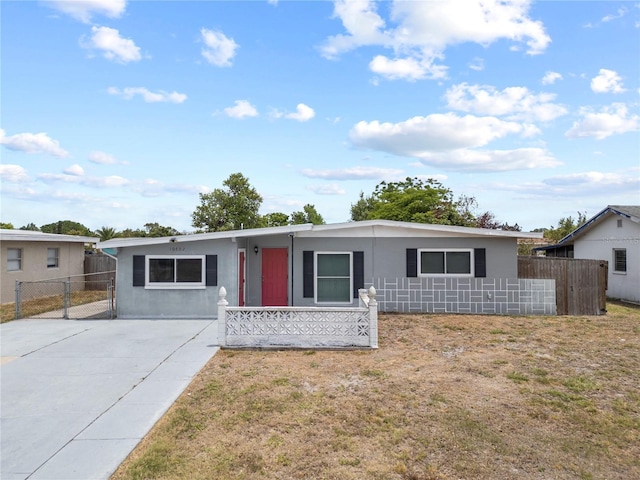 ranch-style house with concrete driveway, stucco siding, fence, and a front lawn