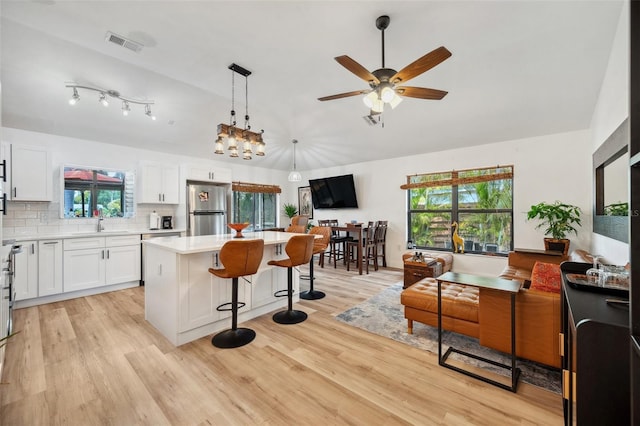 kitchen with a sink, freestanding refrigerator, a breakfast bar area, visible vents, and a kitchen island