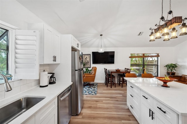 kitchen featuring light wood finished floors, a sink, pendant lighting, visible vents, and appliances with stainless steel finishes
