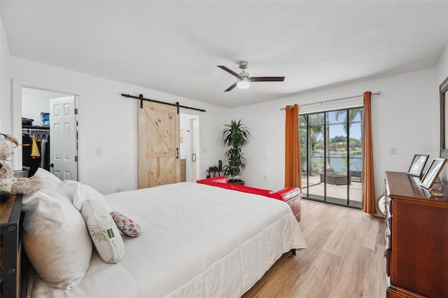 bedroom with a barn door, ceiling fan, light wood-style flooring, a water view, and access to exterior