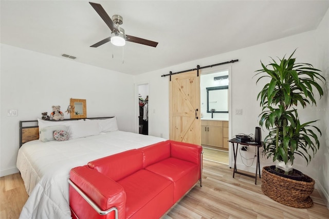 bedroom featuring visible vents, a barn door, ensuite bathroom, ceiling fan, and light wood-style floors