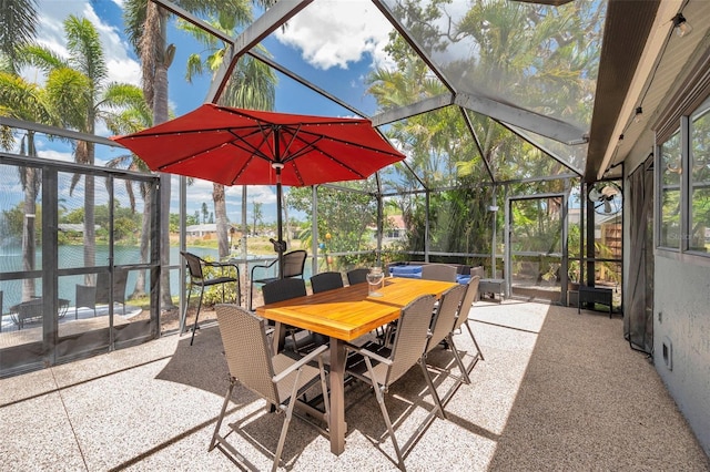 view of patio with a water view, outdoor dining space, and glass enclosure