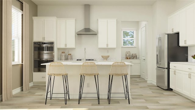 6909 E 116th Ct, Palmetto, FL 34221 - kitchen with light wood finished floors, a kitchen bar, an island with sink, wall chimney range hood, and appliances with stainless steel finishes