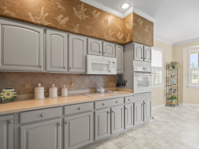 kitchen with white appliances, gray cabinetry, baseboards, decorative backsplash, and crown molding