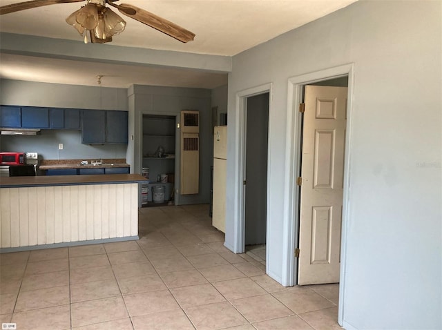 kitchen with dark countertops, ceiling fan, light tile patterned floors, freestanding refrigerator, and a peninsula