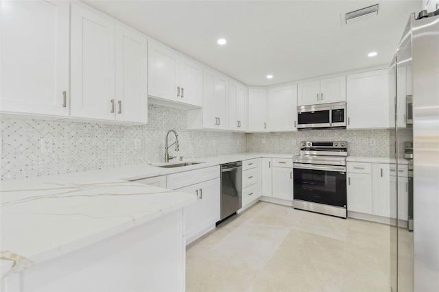 kitchen featuring stainless steel appliances, a sink, light stone counters, white cabinets, and backsplash