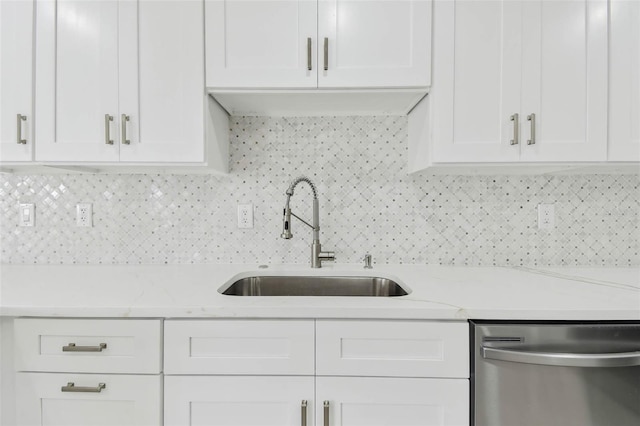 kitchen with stainless steel dishwasher, a sink, white cabinets, decorative backsplash, and light stone counters