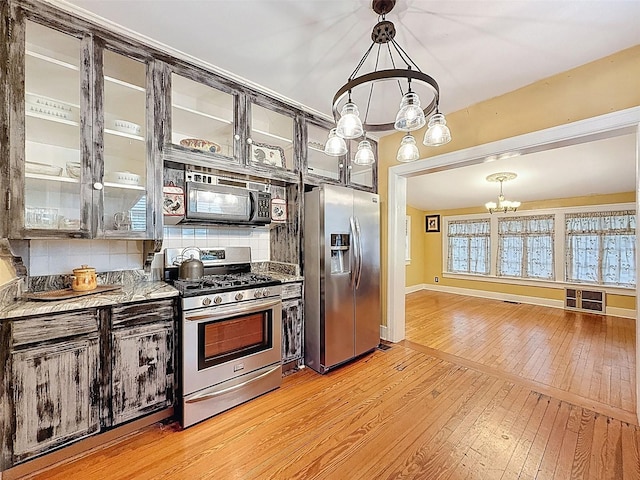800 W Lake Elbert Dr NE, Winter Haven, FL 33881 - kitchen with stainless steel appliances, a chandelier, light wood finished floors, decorative backsplash, and glass insert cabinets