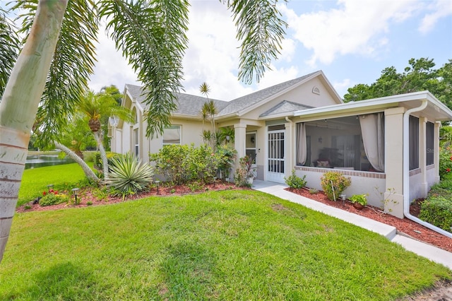 ranch-style home with a sunroom, a front lawn, stucco siding, and a shingled roof
