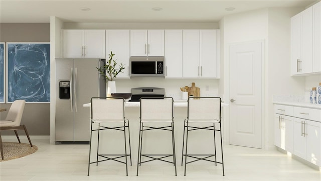 kitchen featuring stainless steel appliances, a center island, a breakfast bar, white cabinetry, and light countertops