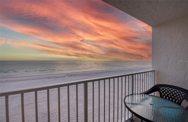 balcony at dusk featuring a water view and a view of the beach