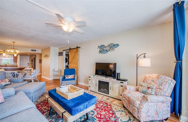 living area featuring ceiling fan with notable chandelier, a textured ceiling, a barn door, visible vents, and baseboards