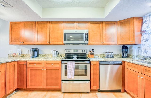 kitchen featuring brown cabinets, light stone counters, light tile patterned floors, and appliances with stainless steel finishes