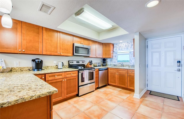 kitchen with light stone countertops, brown cabinetry, visible vents, a sink, and appliances with stainless steel finishes