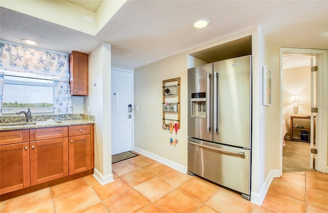 kitchen featuring a sink, brown cabinetry, light tile patterned flooring, baseboards, and stainless steel fridge with ice dispenser