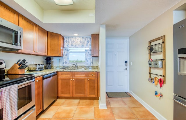 kitchen with light tile patterned floors, brown cabinets, appliances with stainless steel finishes, and a sink