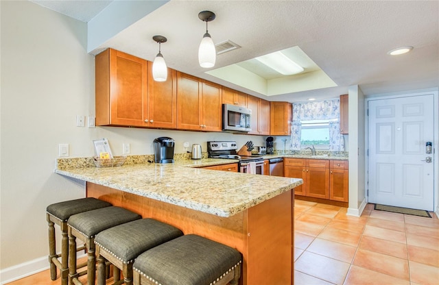 kitchen featuring a peninsula, a breakfast bar area, stainless steel appliances, brown cabinetry, and visible vents