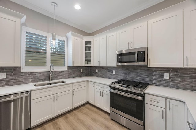kitchen with a sink, stainless steel appliances, white cabinetry, light countertops, and light wood-style floors