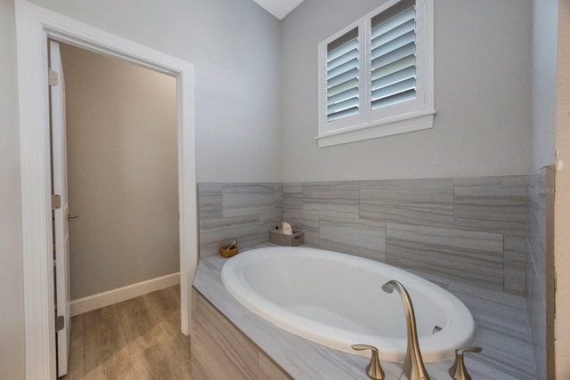 full bath featuring baseboards, a bath, and wood finished floors