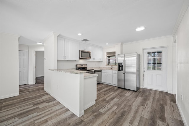 kitchen with stainless steel appliances, white cabinets, crown molding, and wood finished floors