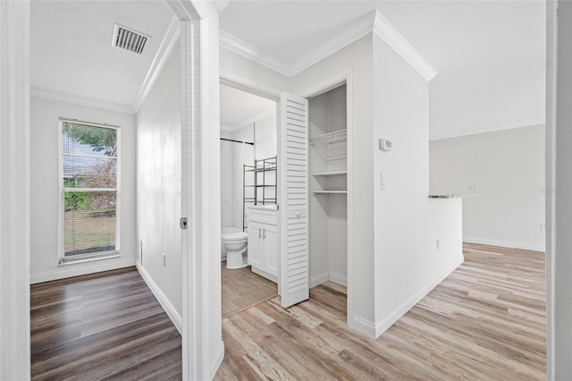 hallway featuring visible vents, wood finished floors, baseboards, and ornamental molding